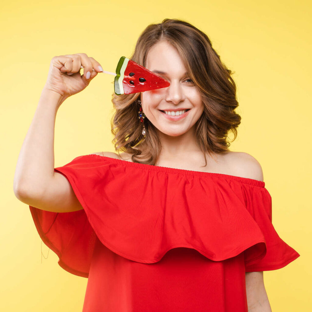 close-up-portrait-attractive-lovely-girl-light-dress-handing-lolipop-isolated-yellow-background_Easy-Resize.com_-1024x1024 Nutrição - Dicas para aproveitar o carnaval com saúde e energia